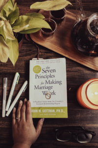 Flatlay of the relationship book Seven Principles of Making a Marriage Work by John Gottman. Photo is surrounded by highlighters, a candle, tea, and a plant.
