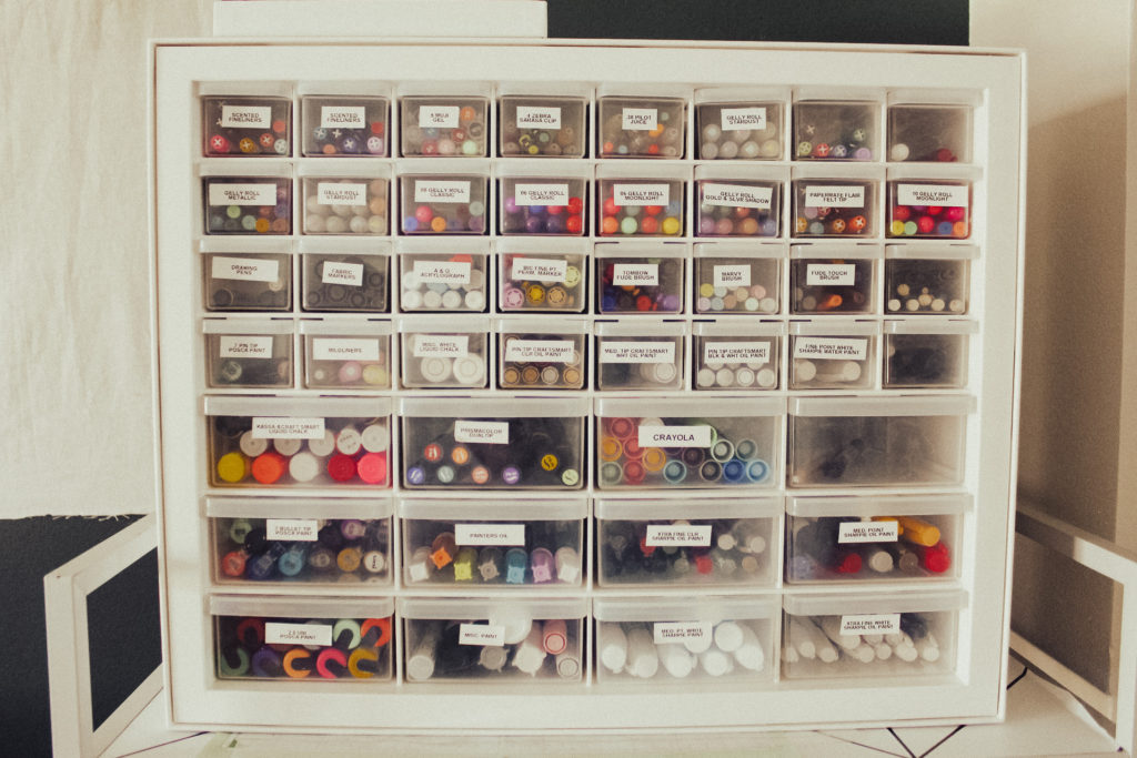 Photo of a multi-drawered cube storage container with different types of pens and each drawer labeled.