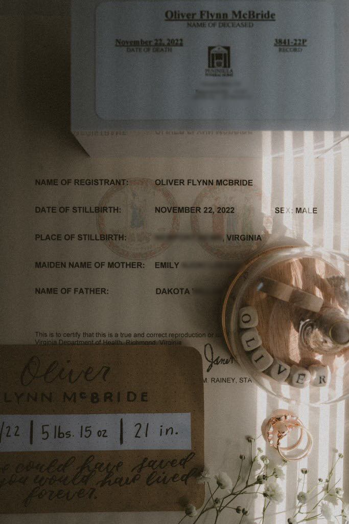 A grief photo honoring my son's stillbirth. A stillbirth certificate is displayed, along with an urn, baby's breath, and breastmilk jewelry.