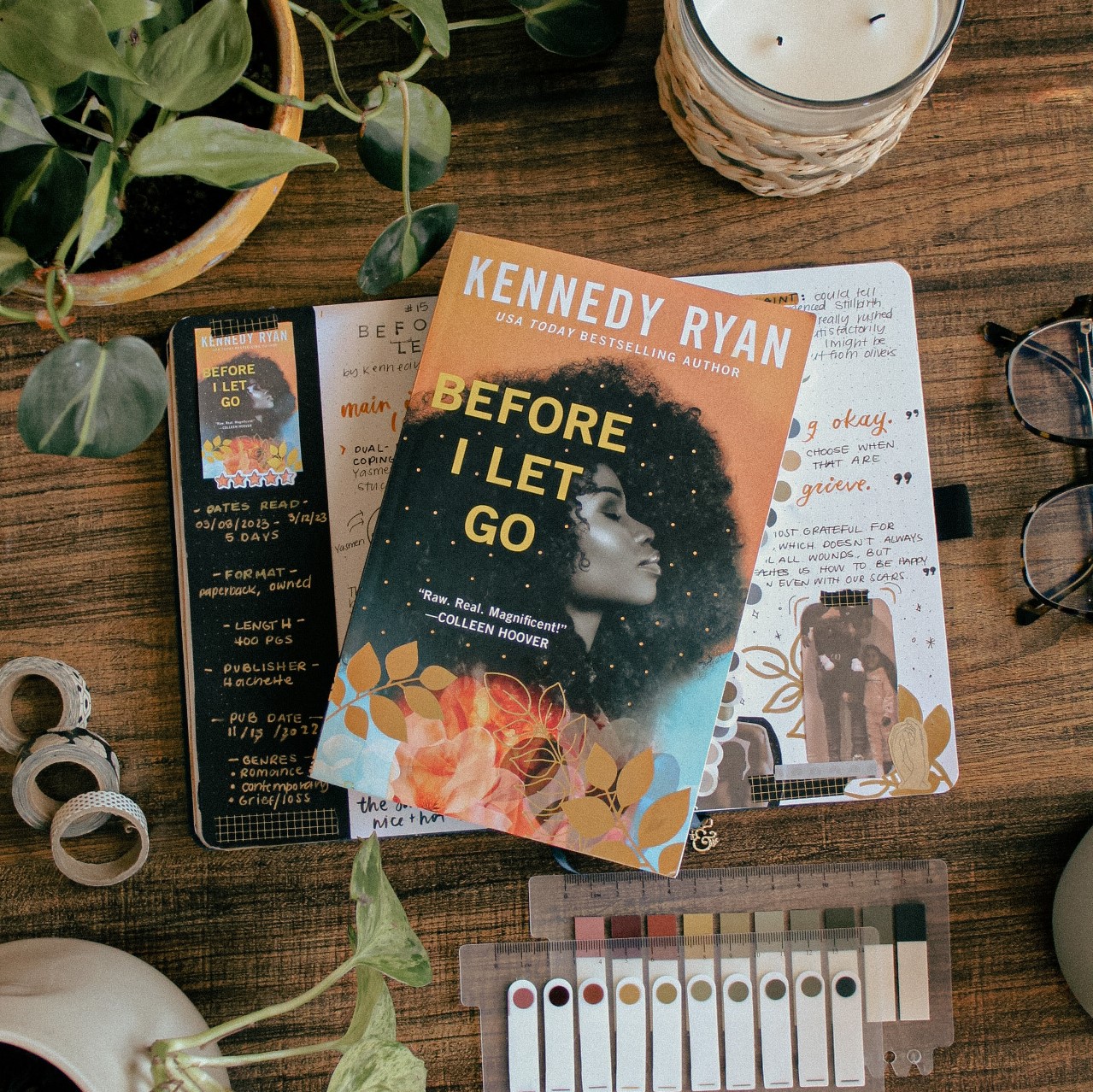 A flat-lay photo of the book Before I Let Go by Kennedy Ryan. The book is lying on a reading journal book review spread for the book. On the table around it are plants and stationery elements.