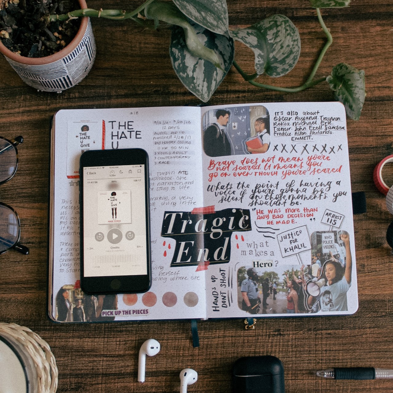 A flat-lay photo of the book The Hate U Give by Angie Thomas. The book is lying on a reading journal book review spread for the book. On the table around it are plants and stationery elements.