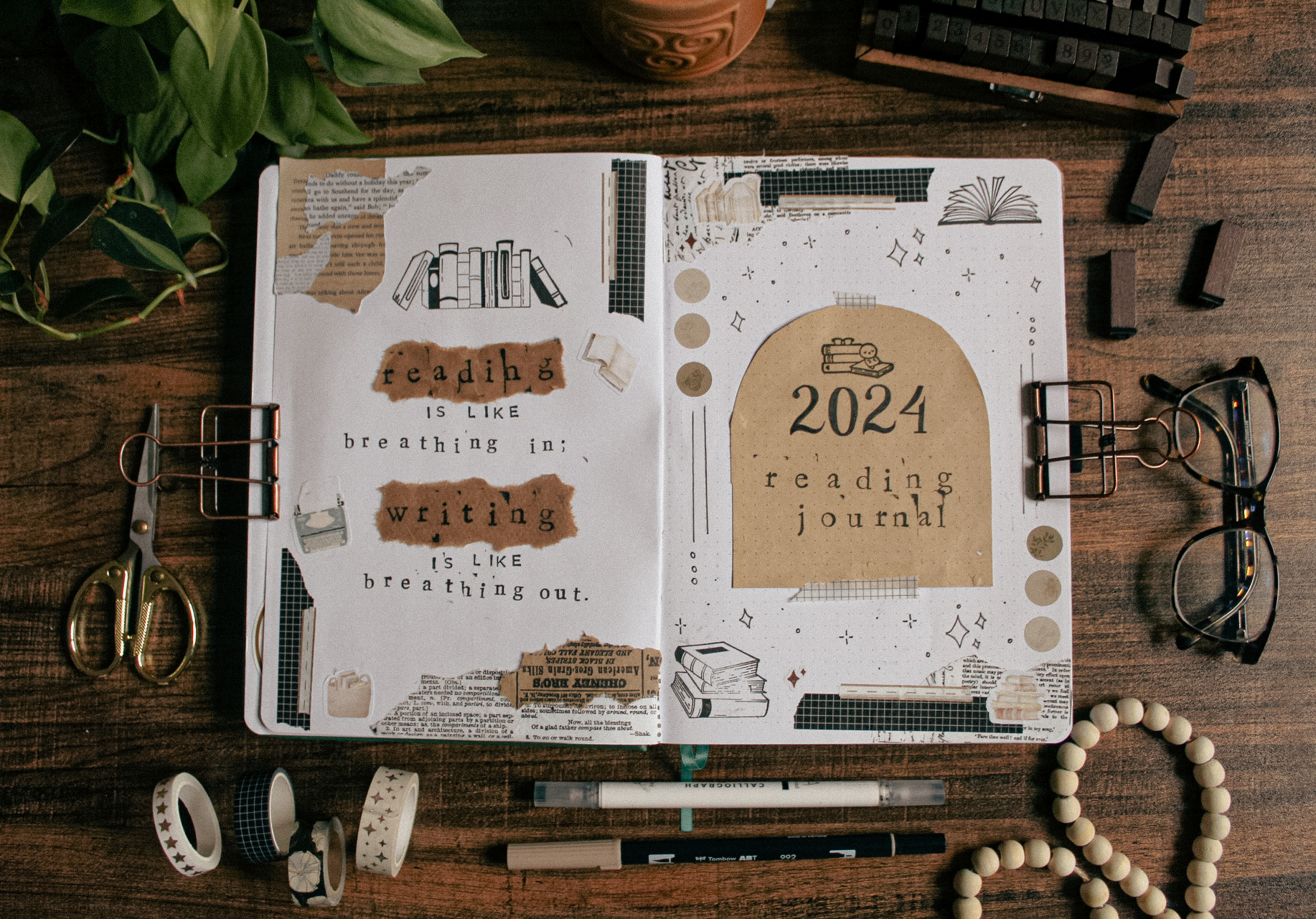 A spread idea for a 2024 reading journal cover page is open on a table surrounded by various decorative and stationery elements.