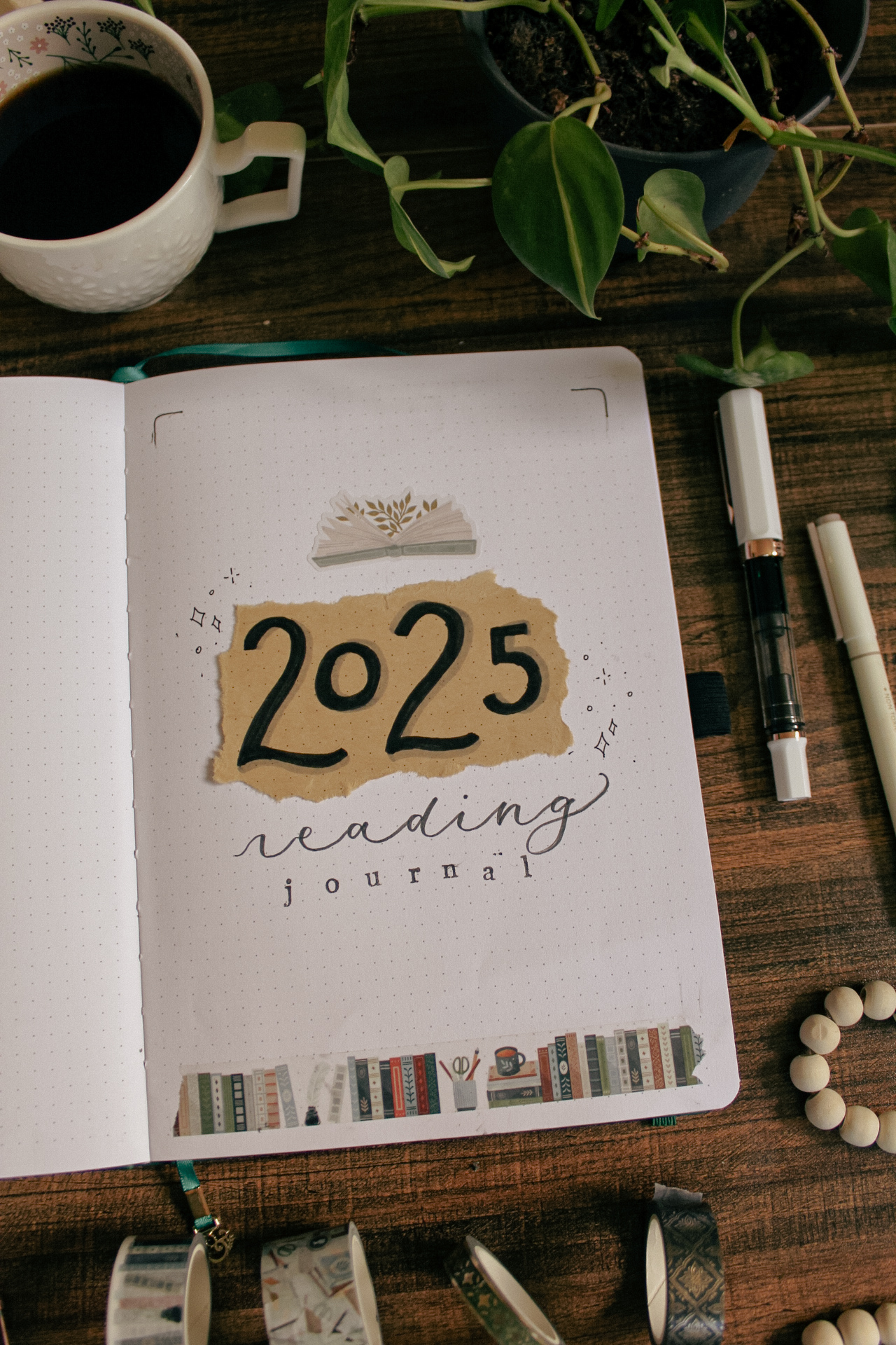 A notebook is open on a desk to Emily's 2025 reading journal cover page. Various decorative and stationery elements are on the desk around the reading journal.