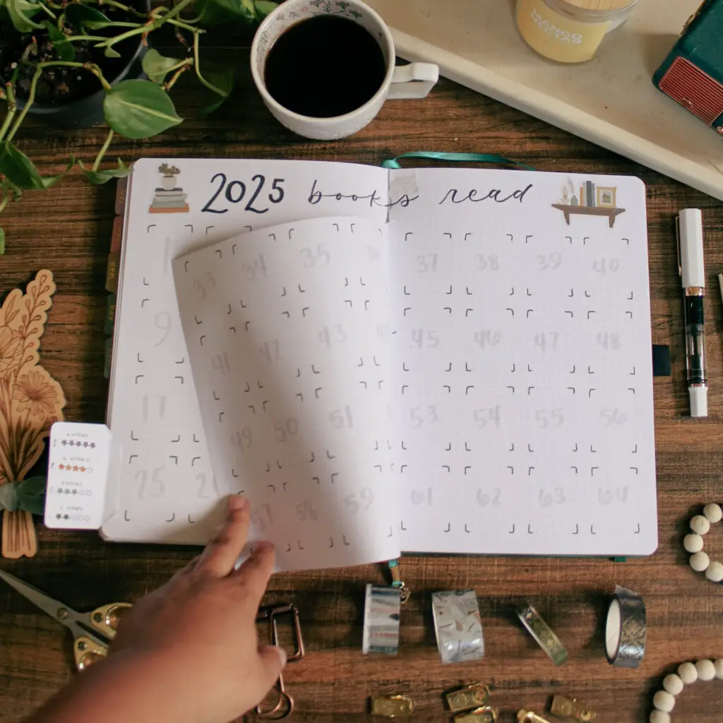 A notebook is open to a page titled 2025 Books Read in a reading journal. A hand is flipping the dutch door in the middle of the page.