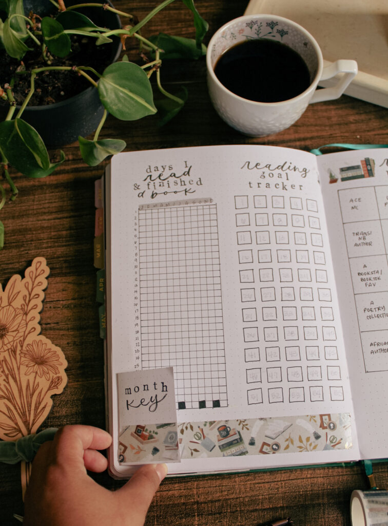 Emily's reading journal is open to a year in pixels page to track days I read and finished a book. On the ride side of the page is a reading goal tracker with 55 squares. There's a tip in pasted onto the left side that says "month key."